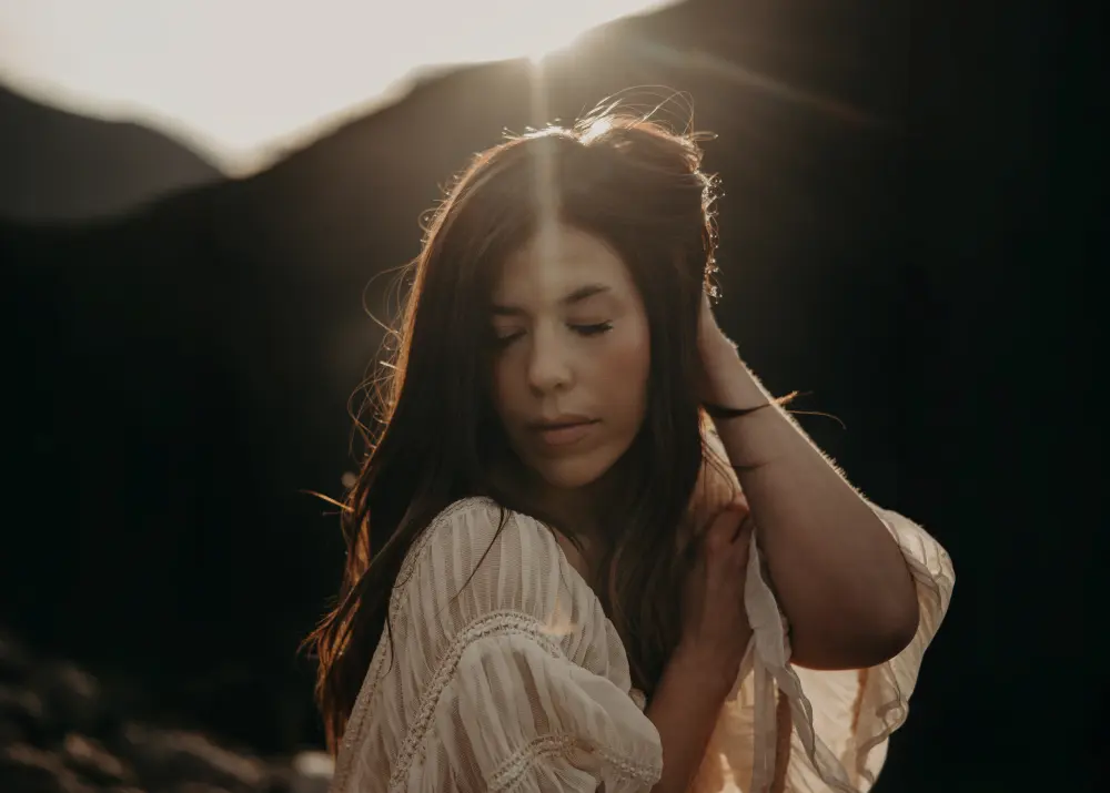 Trudy with her eyes closed and the sun setting behind her over the mountains